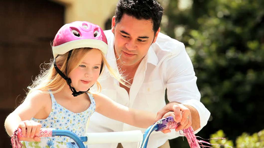 Father helping her daughter in learning how to ride toy wheel Father helping her daughter in learning how to ride toy wheel